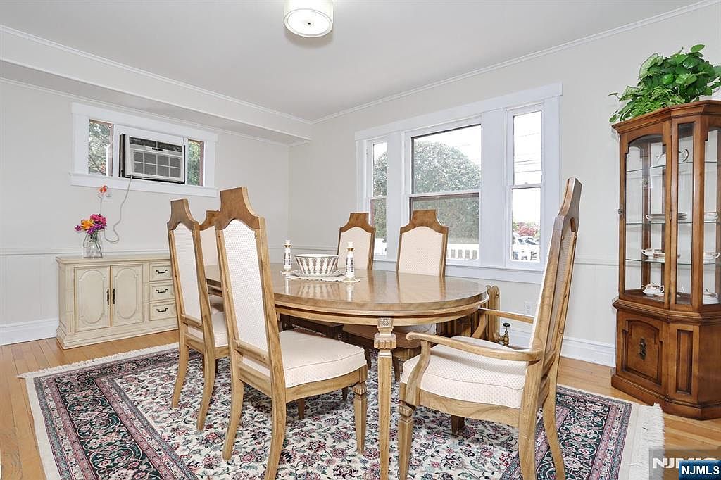 The formal dining room with wainscoting, white crown molding, hardwood floors, and a long oval wood table seating six under a drum-shade pendant light