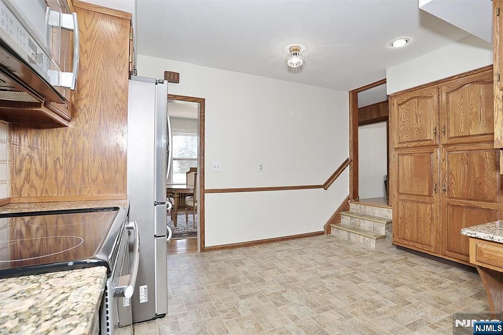 The eat-in kitchen with oak cabinetry, stone-tile floor, stainless steel range and refrigerator, opening to a step-down landing and a glimpse of the adjacent dining room